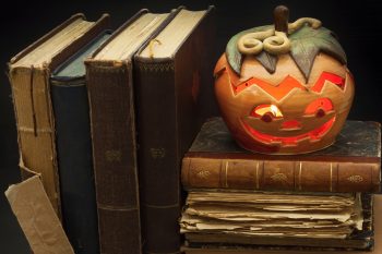 Pumpkin lantern for Halloween and the old witch books. Head carved from a pumpkin on Halloween. Pumpkin tradition. The book of spells, magical book. Textbooks for witches.